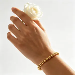 Nahaufnahme eines minimalistischen, 18 Karat vergoldeten 6-mm-Perlenarmbands an der Hand mit Rose