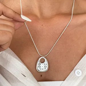 Primo piano di una collana d'argento con pendente ovale perforato indossata.