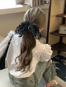 Detail shot showing a black polka dot chiffon bow hair scrunchie tied in a ponytail hairstyle