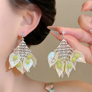 Macro detail of forest style earrings featuring white petals and green cat's eye beads.