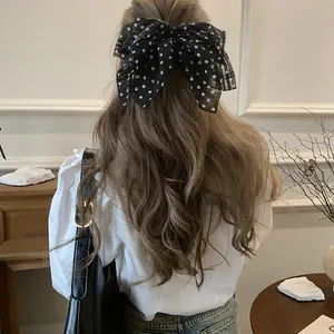 Elegant detail view of a black polka dot chiffon bow hair tie styled on long wavy hair