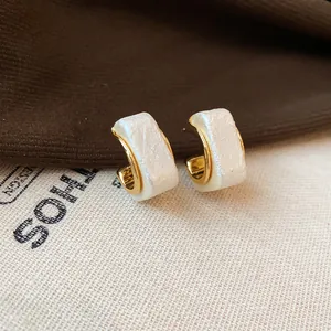 Detailansicht eleganter 18K vergoldeter C-Ohrringe mit strukturierter perlmuttweißer Einlage.