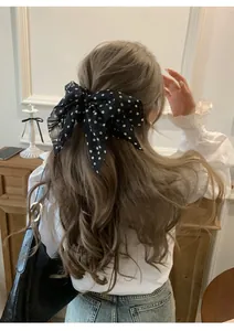 Detail shot of an elegant black polka dot chiffon bow hair tie worn on wavy brown hair