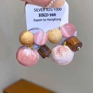 Detailweergave van S925 zilveren naald oorbellen met roze pompons en houten kralen.