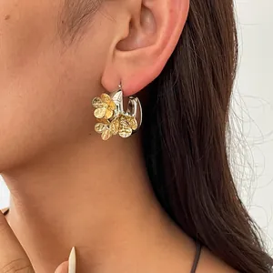 Detailansicht von silbernen Creolen mit strukturierten goldenen Blumenanhängern am Ohr