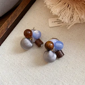 Gedetailleerde weergave van handgemaakte oorbellen met grijze stoffen bollen en hout