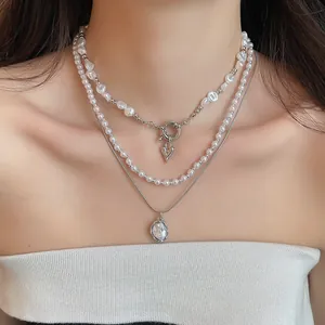 Detailweergave van gelaagde parelkettingen met zilveren hart- en ovale hangers op model.