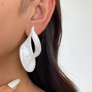 Detailansicht eines unregelmäßigen weißen Emaille-Ohrrings am Ohr des Models