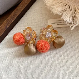 Detailopname van stijlvolle zirkoon bloemoorbellen met oranje en bronzen stoffen bolletjes