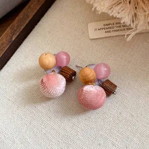 Detailopname van roze pompon oorknopjes met houten kralen en glanzende accenten