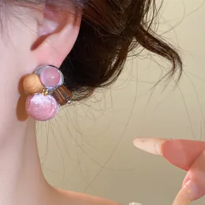 Detailopname van oorbellen van gemengd materiaal met een roze stoffen bal en kralen.