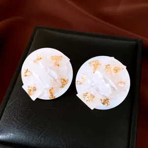 Macro detail of round stud earrings featuring baroque pearls and gold foil accents