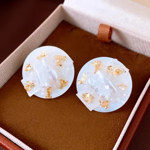 Close-up of elegant circular stud earrings with pearl details and gold leaf accents