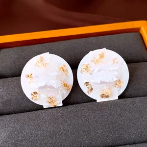 Close-up of elegant round stud earrings with white pearl and gold foil texture