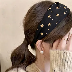 Close-up of a stylish black fabric headband with gold star studs worn by a model