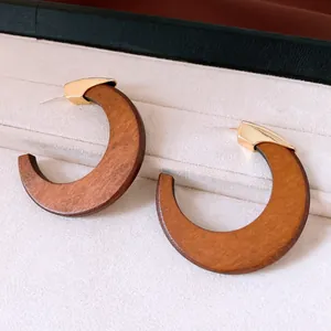 Close-up of retro C-shaped wooden hoop earrings with elegant gold metal accents