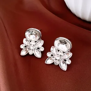 Elegant sparkling silver flower stud earrings with clear oval crystals on luxury brown silk