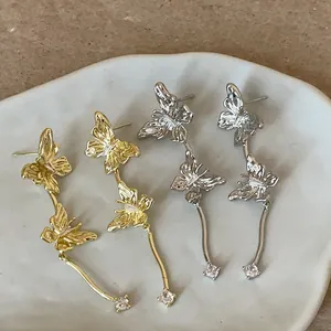 Detailansicht von Schmetterlings-Ohrsteckern mit Quasten und Strass in Gold und Silber.