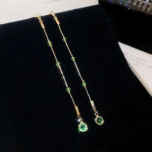 Detailed macro view of elegant long tassel earrings with green crystals on black velvet