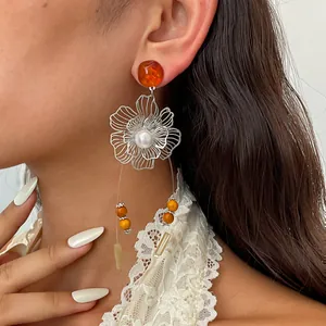 Detailaufnahme von Retro-Metall-Hohlblumenohrringen mit Bernsteinharz und weißer Perle