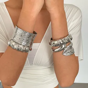 Detailopname van gelaagde zilveren metalen armbanden met getextureerde bladontwerpen.