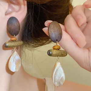 Detailed view of handmade wood and shell teardrop earrings worn by an Asian model