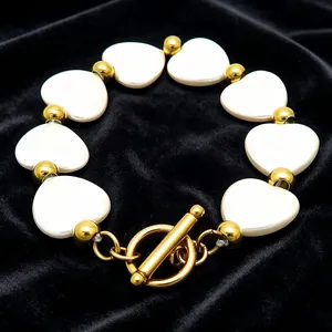Detailansicht eines goldfarbenen OT-Verschlusses und weißer Muschel-Herzperlen auf einem Armband