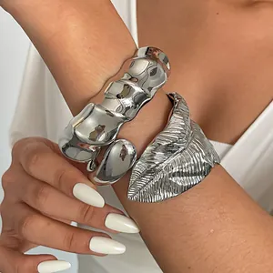 Detailopname van grove zilveren bladmanchetten en vervormde metalen armbanden op de arm