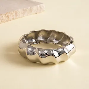 Detailopname van een dikke zilveren metalen armband met onregelmatige plooitexturen.