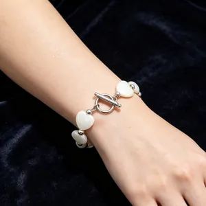 Detailaufnahme eines Armbands aus weißen Herzmuschelperlen mit Stahl-OT-Verschluss am Handgelenk.