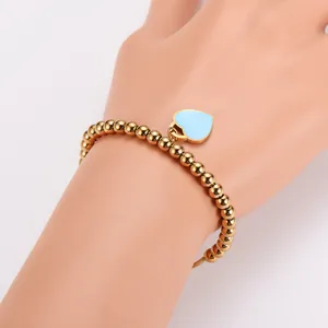 Goldene Edelstahl-Perlenarmband mit blauem Emaille-Herz am Handgelenk im Detail