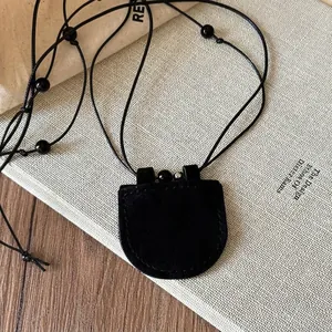 Minimalistische schwarze Lederbrillenhalter-Kette mit rundem Anhänger auf Buch