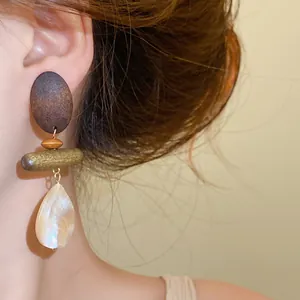 Close-up view of vintage wood and shell teardrop pendant earrings worn by a model
