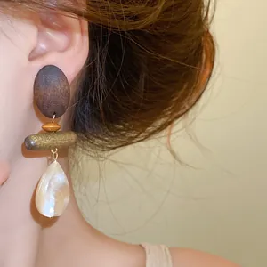 Detailed view of vintage ethnic style wooden and shell teardrop earrings worn on ear