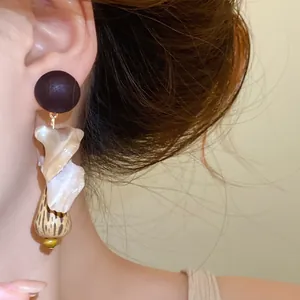 Close-up of vintage ethnic drop earring featuring wood, shell, and water drop pendant