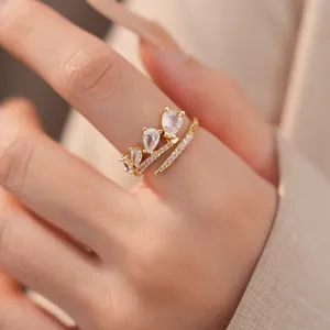 Detail van een elegante gouden open ring met druppelvormige zirkonia en kristallen.