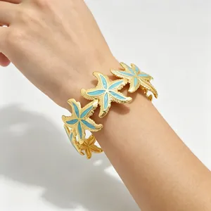 Goldener Ozean-Seestern-Armreif mit blauem Emaille an einem weiblichen Handgelenk.