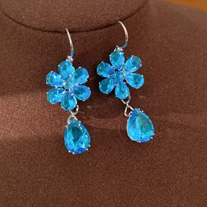 Primo piano di orecchini a fiore e goccia in zircone blu su supporto di velluto.