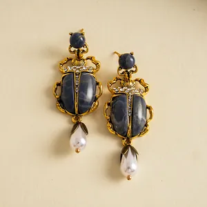 Gros plan sur les boucles d'oreilles scarabées avec pierres et perles gouttes