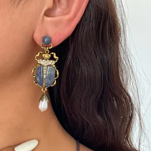 Gros plan d'une boucle d'oreille scarabée dorée vintage avec goutte de perle sur oreille
