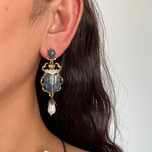 Détail d'une boucle d'oreille scarabée vintage avec pierres bleues et perle sur l'oreille