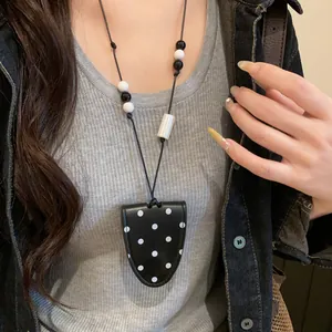 Detail view of a black polka dot leather magnetic glasses holder necklace on a model.