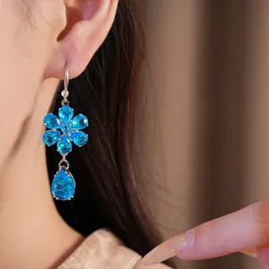 Primo piano di un orecchino a fiore e goccia con zirconi blu indossato da una modella