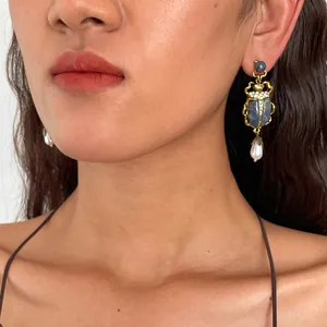 Détail d'une boucle d'oreille scarabée vintage avec pierre bleue et perle sur modèle.