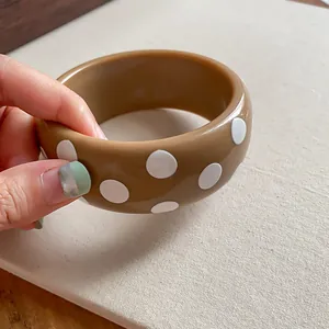 Detailaufnahme eines braunen Y2K-Resin-Armreifs mit trendigem weißen Polka-Dot-Muster