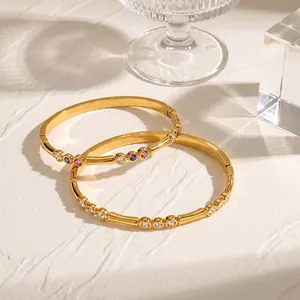 Elegante Nahaufnahme vergoldeter Edelstahlarmbänder mit bunten Zirkonia-Steinen auf Textur