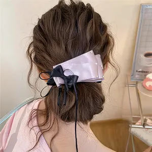 Back view of a pink satin bow hair clip with rhinestones in a brown bun hairstyle.