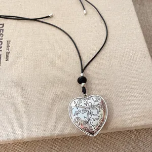 Gros plan d'un pendentif cœur en argent avec gravure florale sur un cordon noir