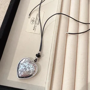 Gros plan détaillé d'un pendentif cœur en argent gravé sur un collier en cordon noir.