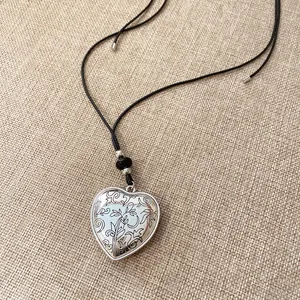 Détail d'un collier avec pendentif coeur gravé et un cordon noir sur un fond de lin.